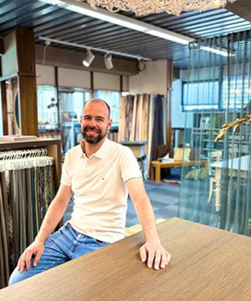 Inhaber Patrick Heckele im Laden an einem Tisch. Dahinter Mustergardinen.